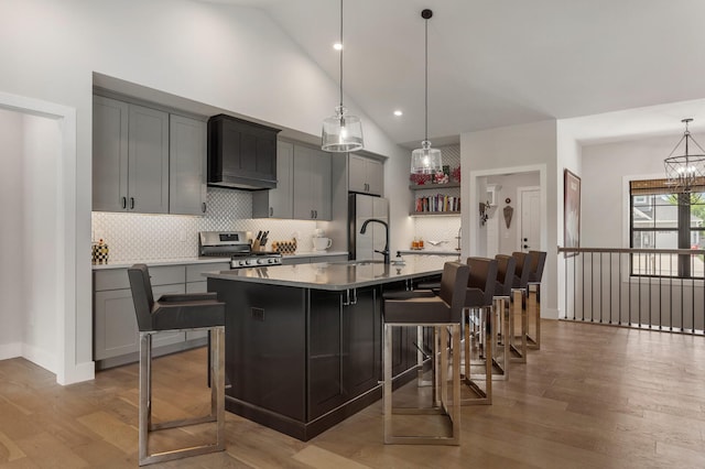 kitchen with appliances with stainless steel finishes, premium range hood, a center island with sink, and light hardwood / wood-style flooring