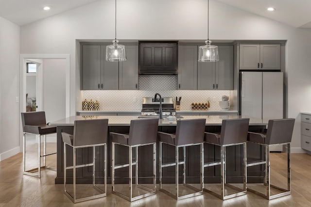 kitchen with decorative light fixtures, white fridge, a kitchen breakfast bar, a kitchen island with sink, and wood-type flooring