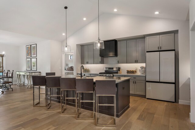 kitchen with light hardwood / wood-style floors, stainless steel appliances, backsplash, a center island with sink, and sink