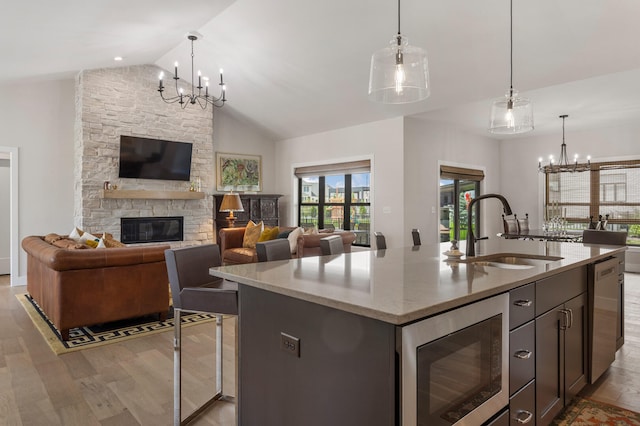 kitchen featuring vaulted ceiling, light hardwood / wood-style floors, a fireplace, stainless steel microwave, and an island with sink