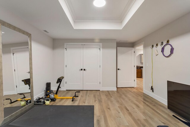 workout room with a tray ceiling and light hardwood / wood-style flooring