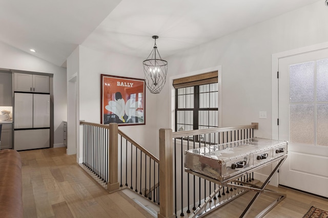 hallway with a notable chandelier, light hardwood / wood-style floors, and lofted ceiling