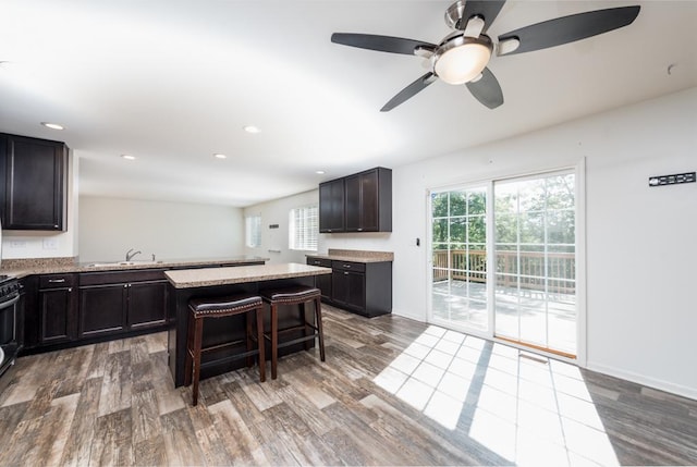 kitchen featuring a center island, dark brown cabinetry, a kitchen bar, and wood finished floors