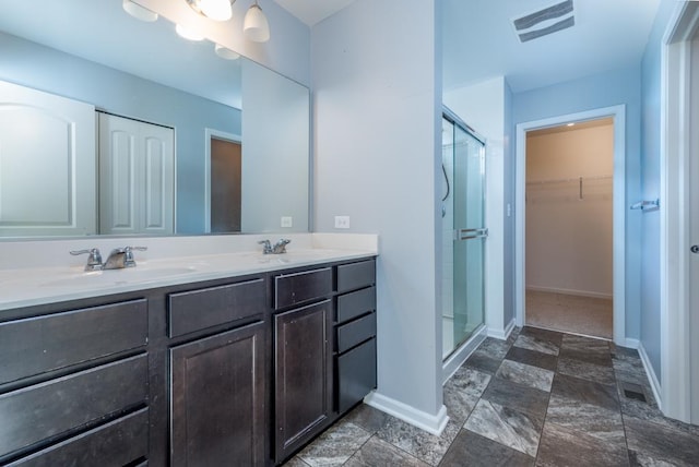 bathroom featuring a walk in closet, visible vents, a sink, a shower stall, and baseboards