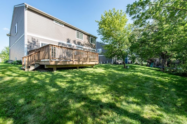 rear view of property with a trampoline, a yard, and a wooden deck