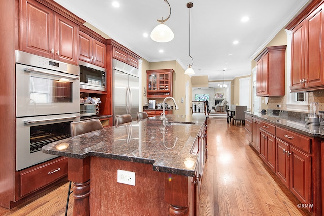 kitchen with sink, an island with sink, light hardwood / wood-style flooring, and built in appliances