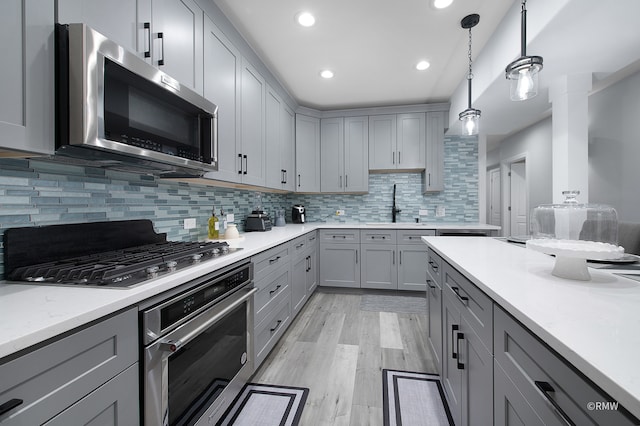 kitchen featuring hanging light fixtures, light hardwood / wood-style flooring, appliances with stainless steel finishes, sink, and tasteful backsplash