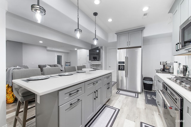 kitchen with light hardwood / wood-style floors, stainless steel appliances, pendant lighting, a kitchen island, and a breakfast bar area