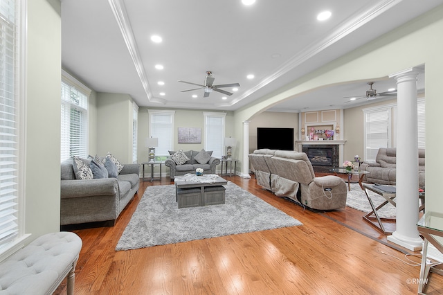 living room featuring decorative columns, hardwood / wood-style floors, ceiling fan, and a tray ceiling