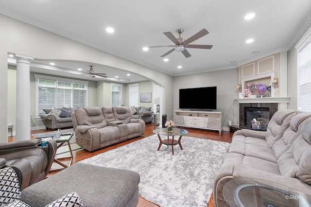 living room featuring ceiling fan, crown molding, ornate columns, a fireplace, and dark wood-type flooring