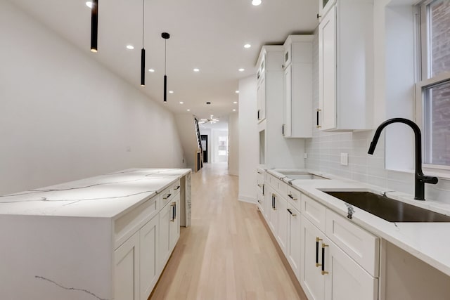 kitchen featuring light hardwood / wood-style floors, backsplash, white cabinetry, sink, and pendant lighting