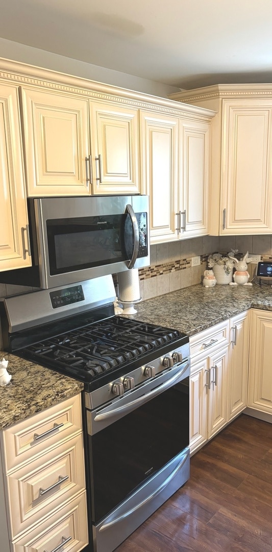 kitchen with dark hardwood / wood-style flooring, dark stone counters, range with gas stovetop, cream cabinets, and tasteful backsplash