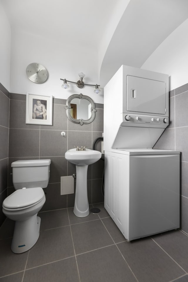 bathroom featuring tile flooring, stacked washer and clothes dryer, and tile walls