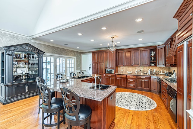 kitchen featuring an island with sink, sink, light hardwood / wood-style floors, and ornamental molding