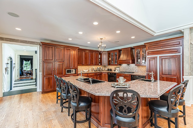 kitchen featuring custom range hood, light hardwood / wood-style flooring, sink, and a large island with sink