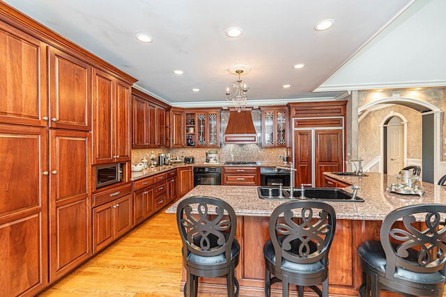 kitchen with custom range hood, light hardwood / wood-style floors, built in appliances, a kitchen bar, and light stone countertops