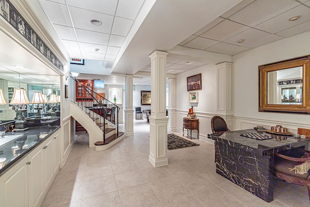 interior space featuring light tile floors, a paneled ceiling, and ornate columns