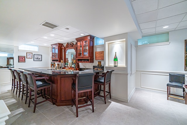 kitchen with a kitchen breakfast bar, kitchen peninsula, light tile floors, and a drop ceiling