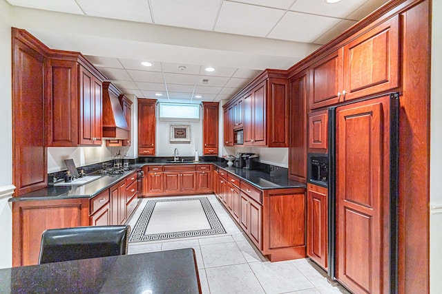 kitchen featuring built in appliances, premium range hood, a drop ceiling, sink, and light tile floors