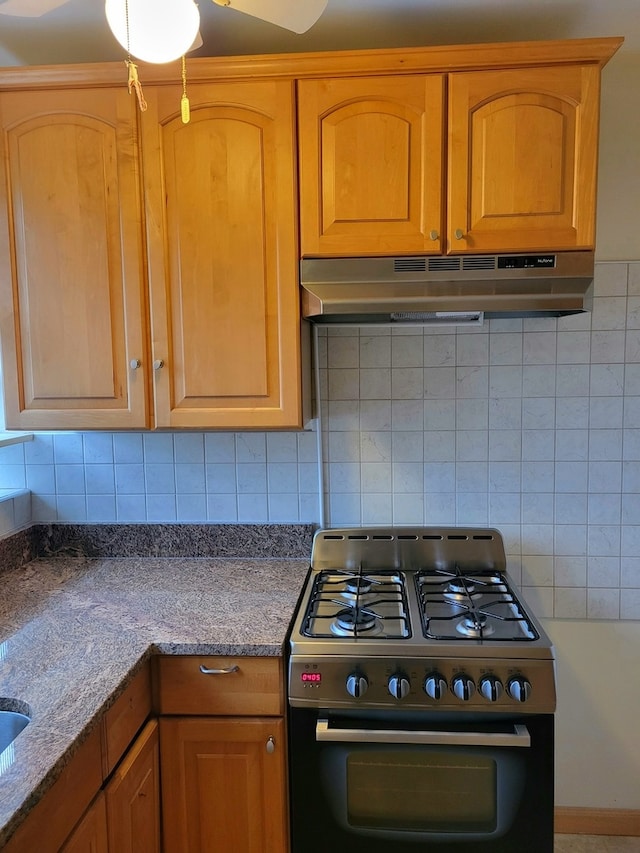 kitchen featuring gas range oven, stone counters, ceiling fan, and backsplash