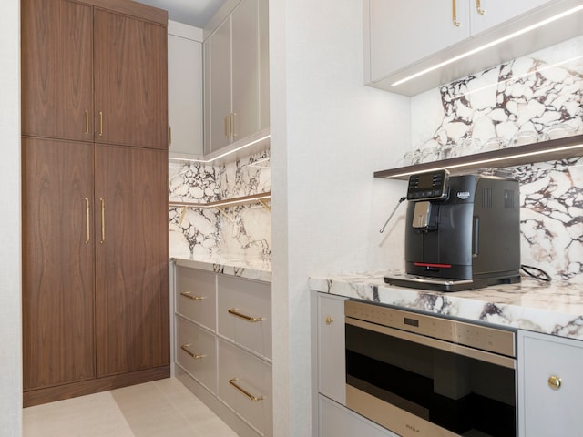 kitchen with tasteful backsplash, white cabinets, oven, light stone counters, and light tile patterned floors