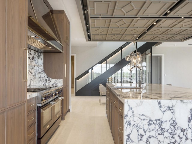 kitchen featuring wall chimney range hood, brown cabinets, range with two ovens, light stone counters, and a sink