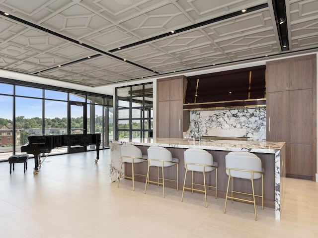 kitchen featuring light stone counters, a sink, expansive windows, a kitchen bar, and modern cabinets