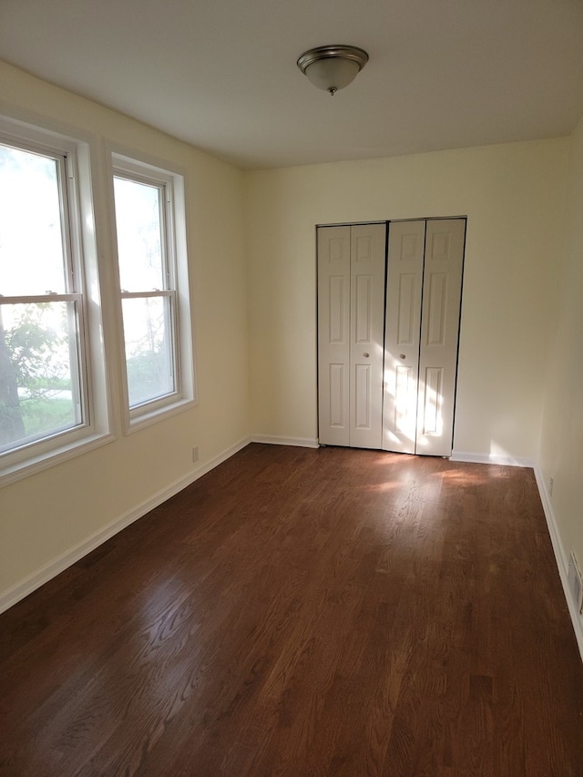 unfurnished bedroom with multiple windows, dark wood-type flooring, and a closet