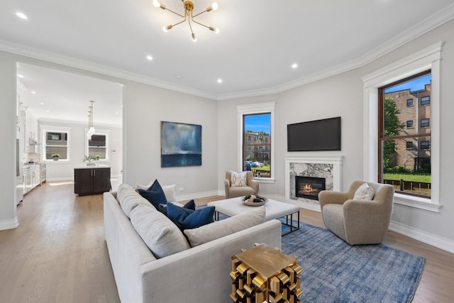 living room with a high end fireplace, an inviting chandelier, crown molding, a wealth of natural light, and light hardwood / wood-style floors