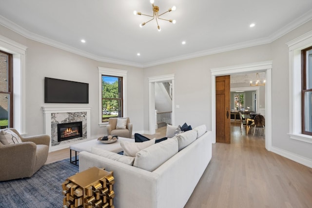 living room featuring a chandelier, light hardwood / wood-style flooring, crown molding, and a premium fireplace