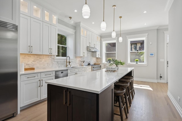 kitchen with premium appliances, a kitchen island, sink, pendant lighting, and white cabinetry