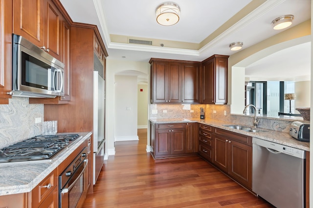 kitchen with sink, dark wood-type flooring, stainless steel appliances, light stone counters, and backsplash