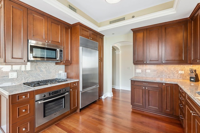 kitchen featuring light wood-type flooring, ornamental molding, appliances with stainless steel finishes, tasteful backsplash, and light stone counters