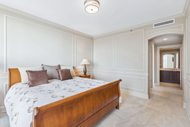 bedroom featuring light colored carpet, ensuite bath, and crown molding