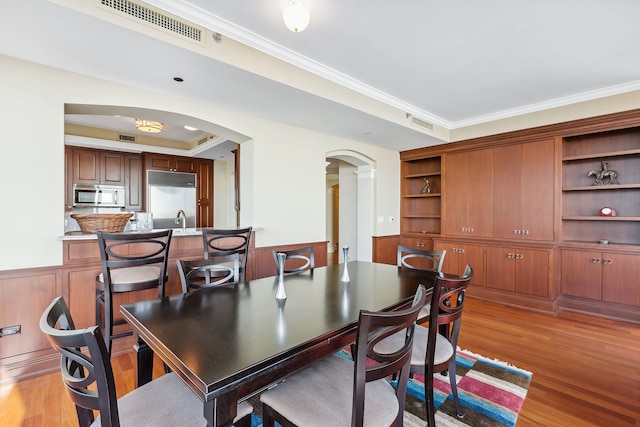 dining space with light hardwood / wood-style flooring, a raised ceiling, crown molding, and sink