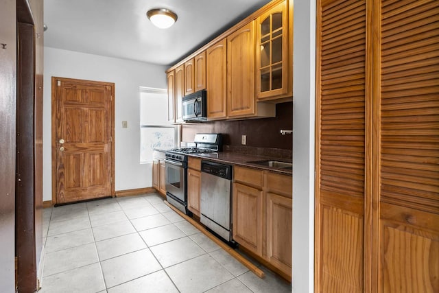 kitchen featuring dark stone counters, sink, light tile patterned floors, and stainless steel appliances