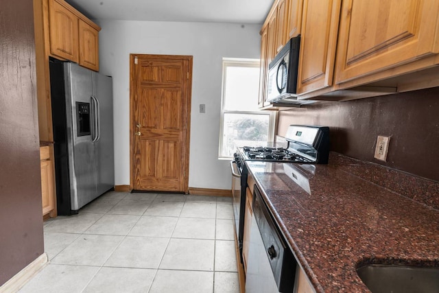 kitchen with gas stove, dishwasher, stainless steel refrigerator with ice dispenser, dark stone countertops, and light tile patterned floors