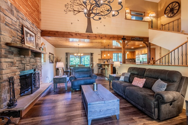 living room with dark hardwood / wood-style floors, a stone fireplace, beam ceiling, a towering ceiling, and a chandelier