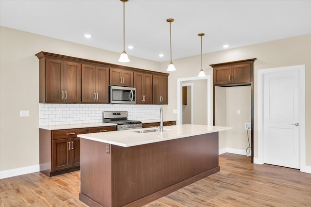 kitchen with appliances with stainless steel finishes, pendant lighting, decorative backsplash, and light wood-type flooring