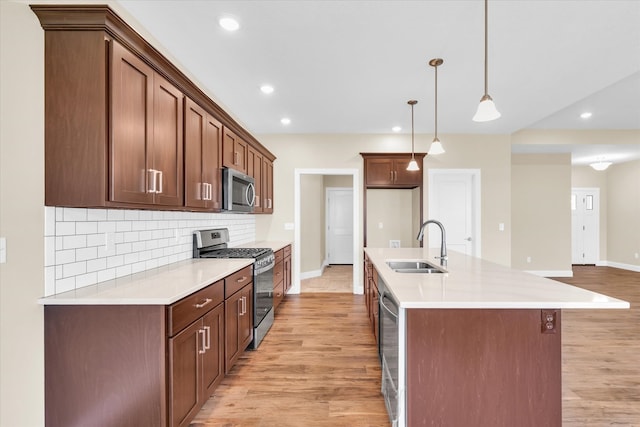 kitchen with appliances with stainless steel finishes, tasteful backsplash, sink, light hardwood / wood-style floors, and decorative light fixtures