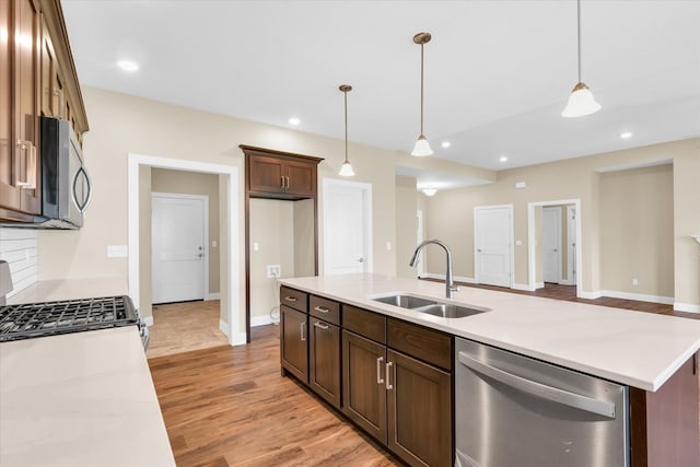 kitchen with sink, light wood-type flooring, stainless steel appliances, and decorative light fixtures