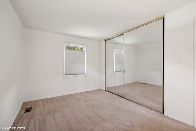 unfurnished bedroom with light colored carpet and a closet