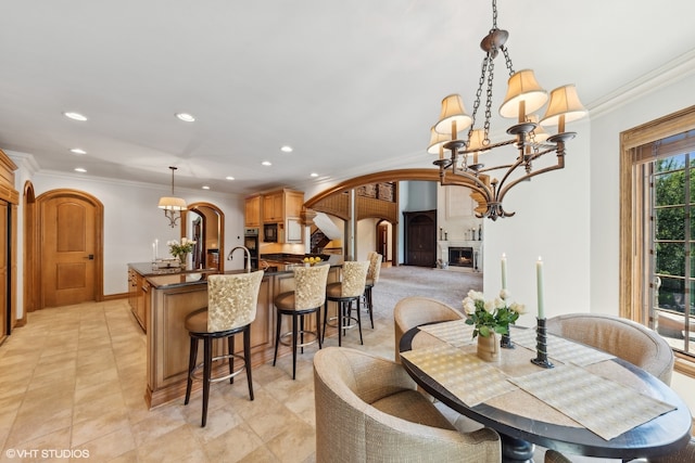 tiled dining area featuring crown molding, sink, a fireplace, and a chandelier