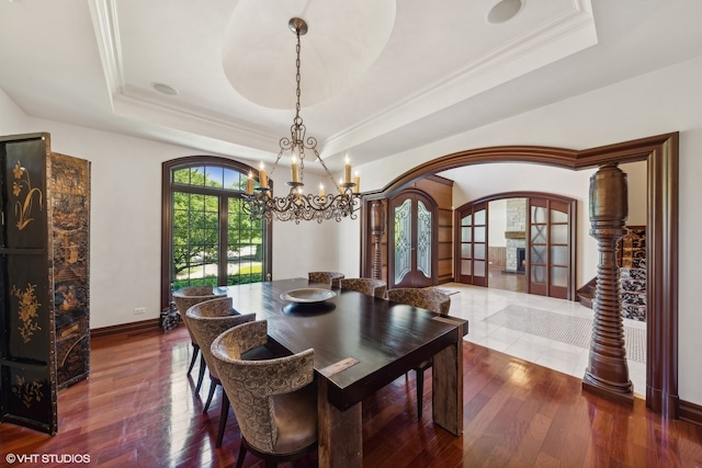 dining room with a raised ceiling, wood-type flooring, a notable chandelier, and french doors