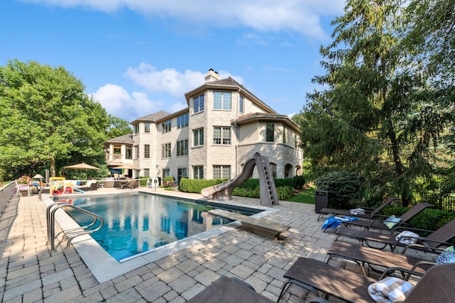 view of pool with a diving board, a water slide, and a patio