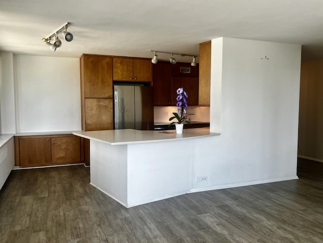 kitchen with dark wood finished floors, freestanding refrigerator, a peninsula, brown cabinetry, and light countertops