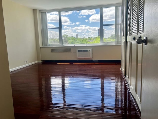 empty room featuring a wall mounted air conditioner, baseboards, a healthy amount of sunlight, and wood finished floors