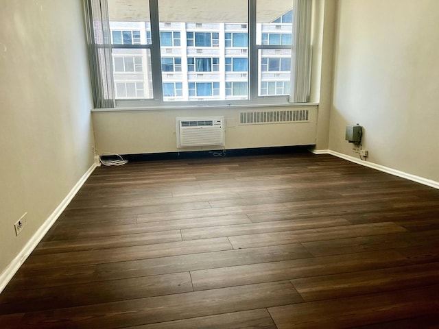 spare room featuring baseboards, an AC wall unit, and dark wood finished floors