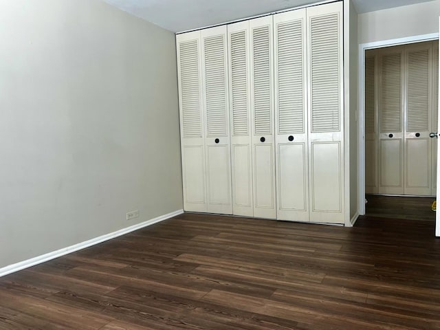 unfurnished bedroom with a closet, baseboards, and dark wood-style flooring