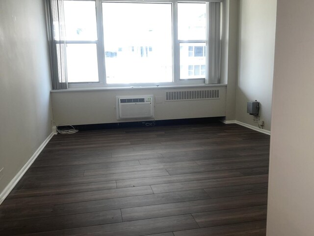 unfurnished room with dark wood-type flooring, plenty of natural light, and an AC wall unit